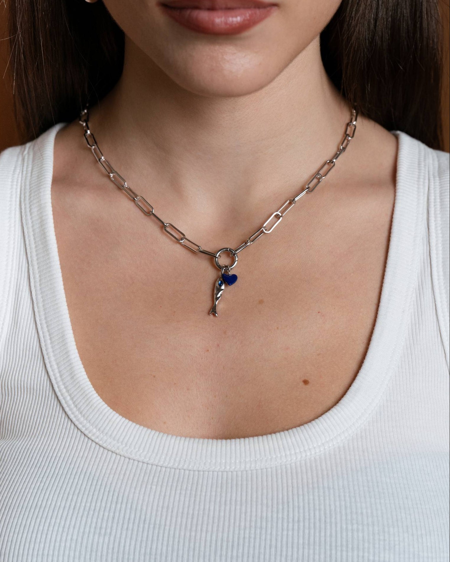 Necklace with a Andie heart-shaped pendant `nd jean molten fish charm worn by a person in a white tank top.