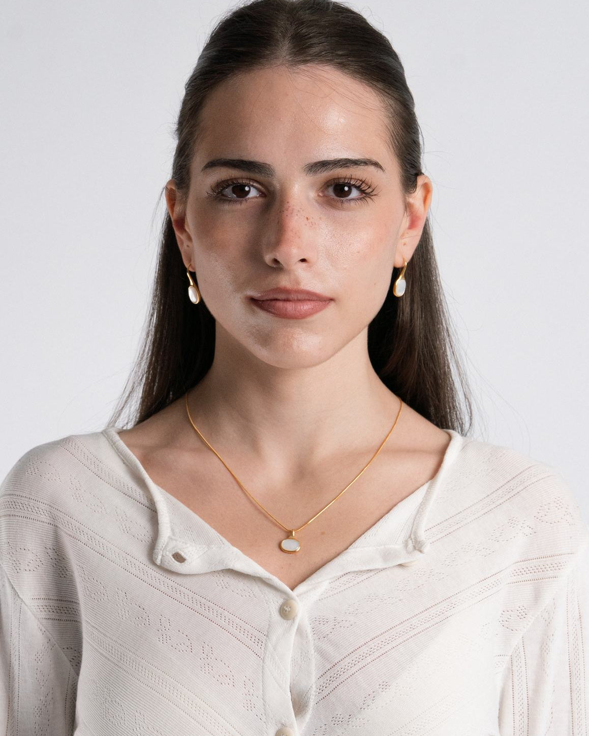 Woman wearing a white shirt with a plain background with 18 plated sigrid shell oval earrings and necklace