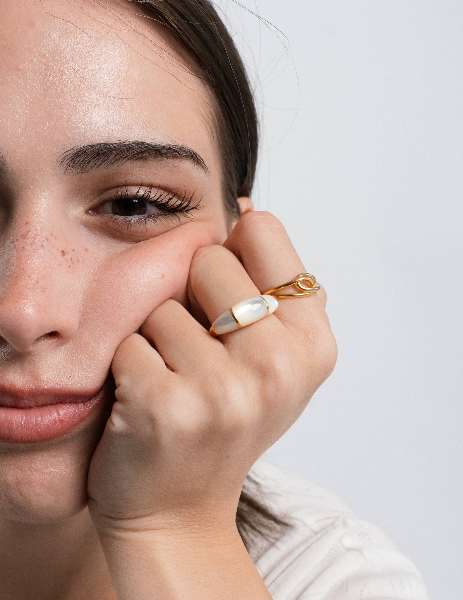 Close-up of a person wearing sigrid dome ring and pom paperclip ring gold rings