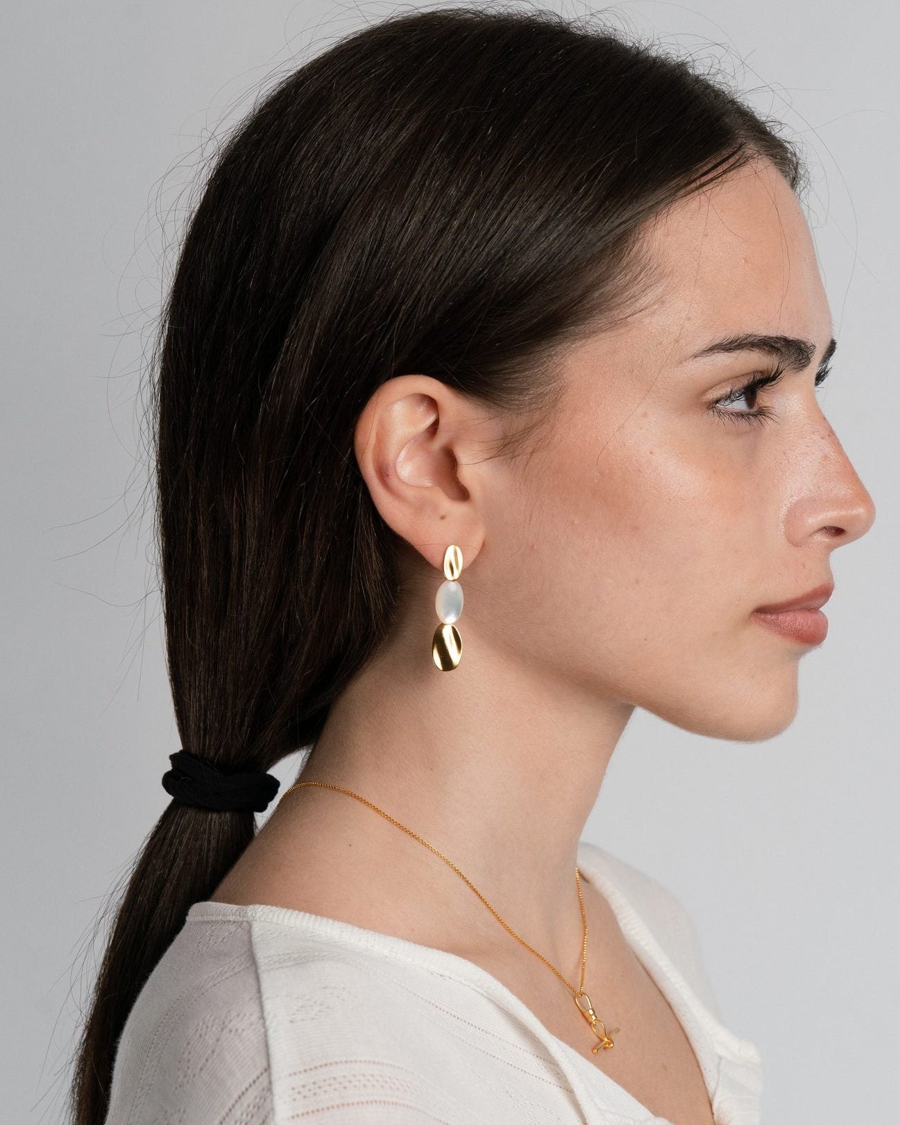 Woman wearing 18k gold sigrid cascade earrings and a necklace against a plain background
