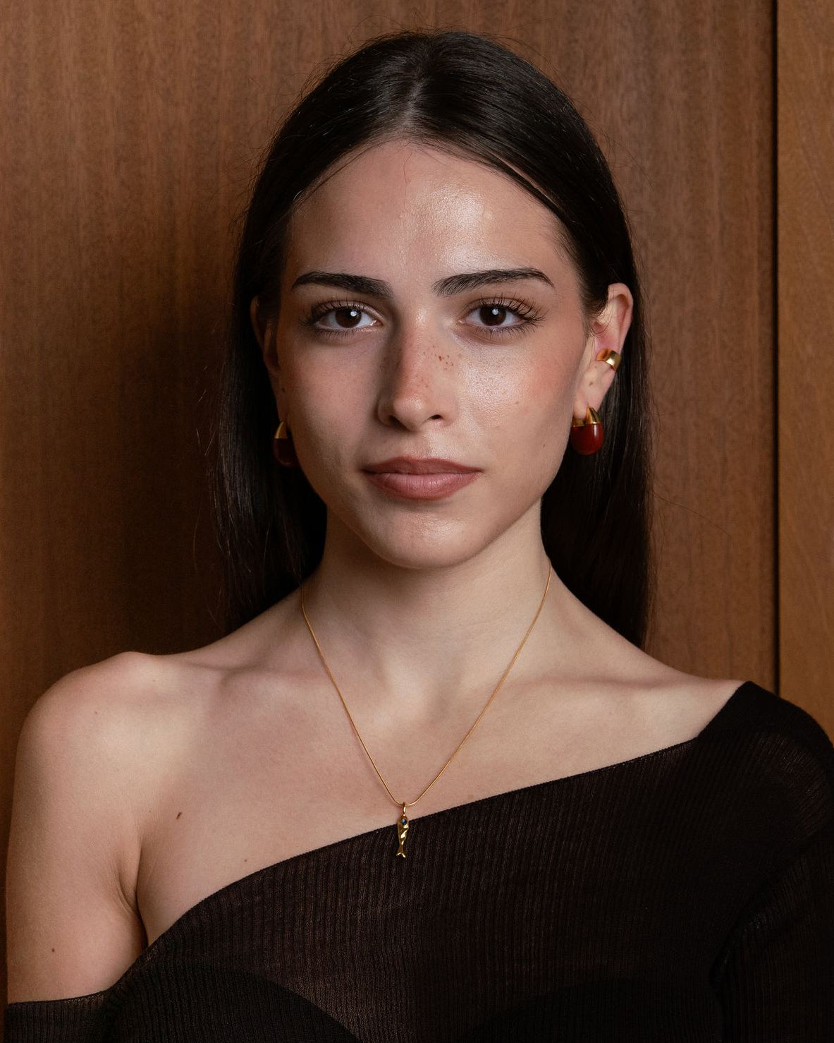 Woman wearing a black off-shoulder top wearing  fish charm necklace and ear cuff and dome earring

