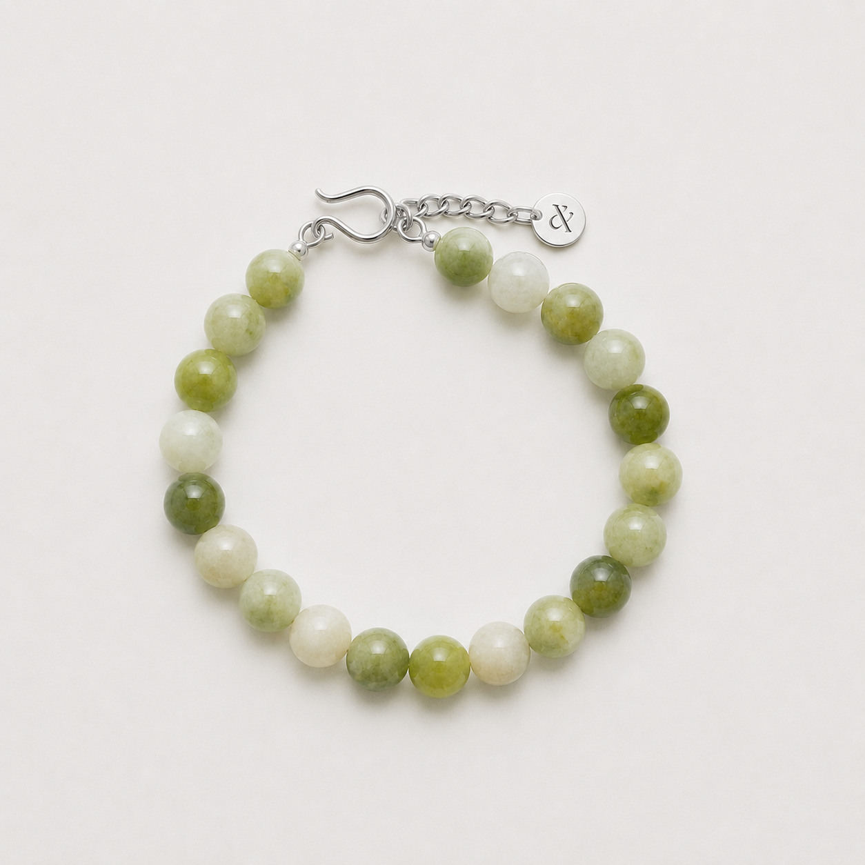A beaded bracelet made of alternating light green and white marbled beads, finished with a silver-tone lobster clasp and extender chain featuring a small round charm engraved with lines & current logo mark
